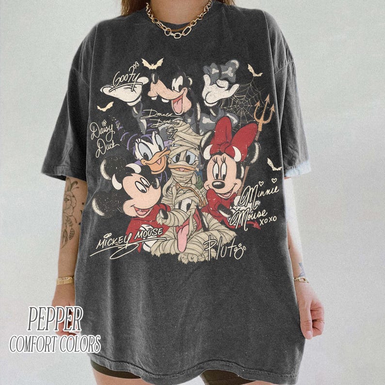May include: Dark grey t-shirt with a graphic of Disney characters, including Mickey Mouse, Minnie Mouse, Donald Duck, and Goofy. The design includes bats, spiderwebs, and the text "Mickey Mouse" and "Minnie Mouse". The shirt also has the text "Pepper Comfort Colors".