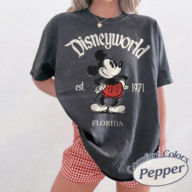 May include: Dark gray t-shirt featuring a classic Mickey Mouse graphic with the text "Disneyworld" above and "est. 1971 FLORIDA" below. The shirt is a Comfort Colors brand.