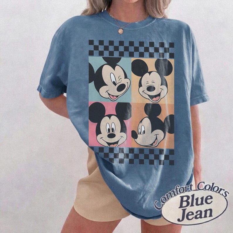 May include: Blue t-shirt featuring four panels with Mickey Mouse's face in different expressions. The panels are set against a checkered background. The shirt has the words "Comfort Colors Blue Jean" printed on it.