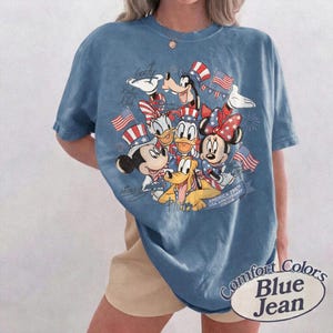 Puede incluir: Camiseta Comfort Colors azul vaquero con un dise&ntilde;o de Mickey Mouse, Minnie Mouse, Donald, Goofy y Pluto con atuendos patri&oacute;ticos. La camiseta tiene el texto "America 250th USA Anniversary 1776-2026".
