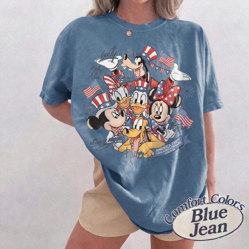 Puede incluir: Camiseta Comfort Colors azul vaquero con un dise&ntilde;o de Mickey Mouse, Minnie Mouse, Donald, Goofy y Pluto con atuendos patri&oacute;ticos. La camiseta tiene el texto "America 250th USA Anniversary 1776-2026".