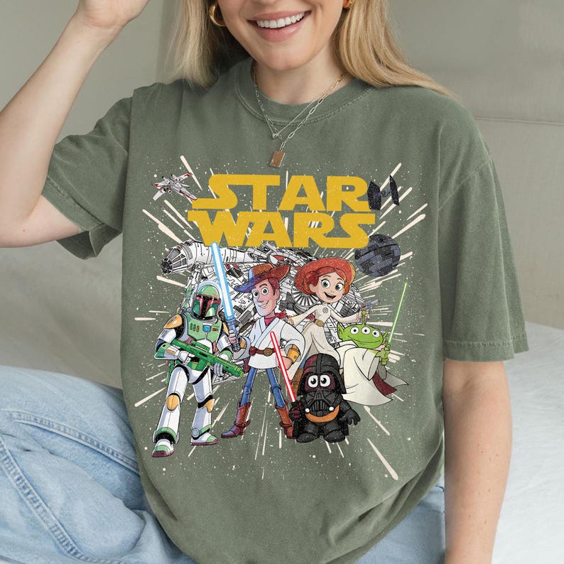 Puede incluir: Camiseta verde oliva con un gr&aacute;fico de personajes de Star Wars, incluyendo a Boba Fett, Woody y Jessie. Las palabras "STAR WARS" est&aacute;n en amarillo. El dise&ntilde;o tiene un aspecto vintage.