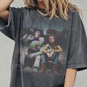 May include: Dark grey oversized t-shirt with a graphic of Buzz Lightyear and Woody from Toy Story. The characters are shown sitting together. The shirt has a vintage, distressed appearance.