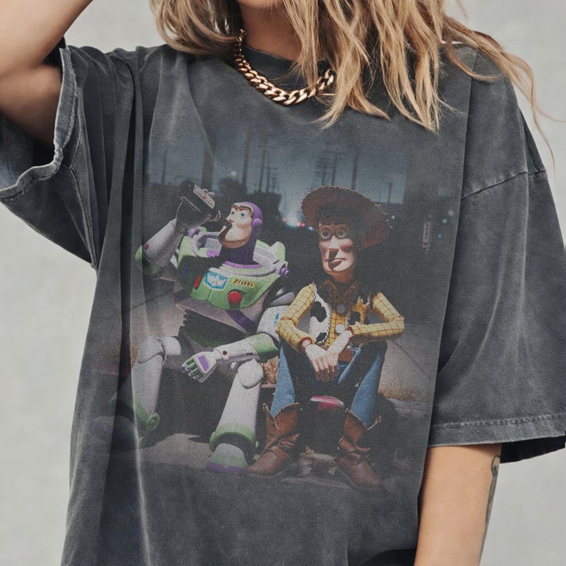 May include: Dark grey oversized t-shirt with a graphic of Buzz Lightyear and Woody from Toy Story. The characters are shown sitting together. The shirt has a vintage, distressed appearance.