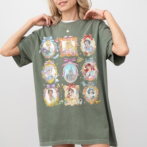 Pu&ograve; includere: T-shirt verde oliva con nove ritratti incorniciati di principesse Disney. Ogni ritratto &egrave; circondato da fiori e fiocchi. Un castello &egrave; al centro. La maglietta ha una vestibilit&agrave; ampia e maniche corte.