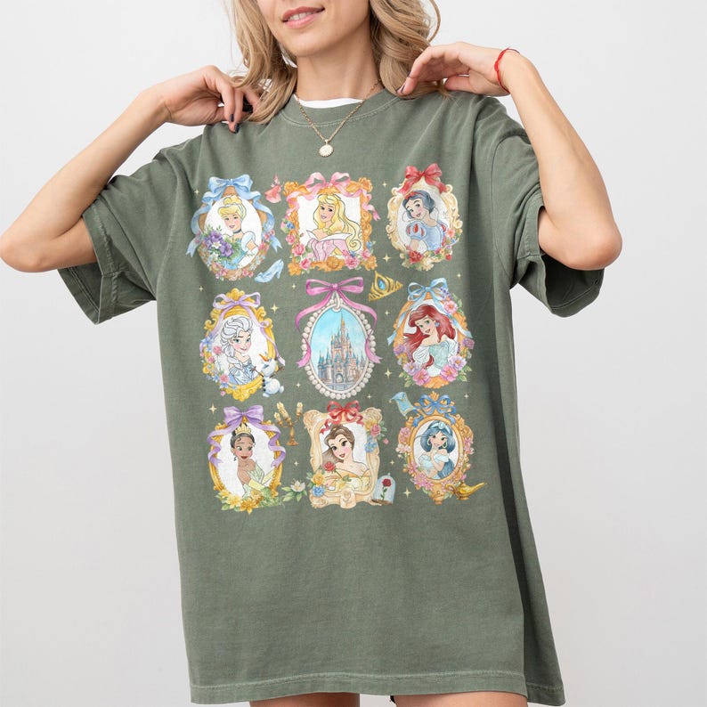 Pu&ograve; includere: T-shirt verde oliva con nove ritratti incorniciati di principesse Disney. Ogni ritratto &egrave; circondato da fiori e fiocchi. Un castello &egrave; al centro. La maglietta ha una vestibilit&agrave; ampia e maniche corte.