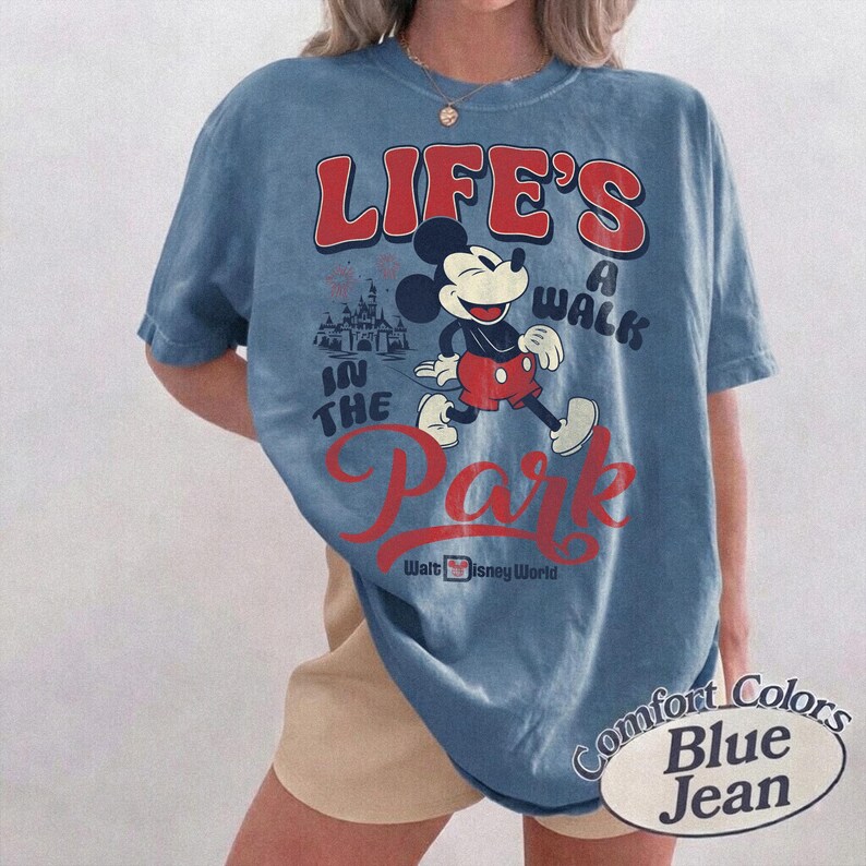 May include: Blue jean Comfort Colors t-shirt featuring Mickey Mouse walking in front of a castle with the text "LIFE'S A WALK IN THE PARK" in red. The shirt also says "Walt Disney World".