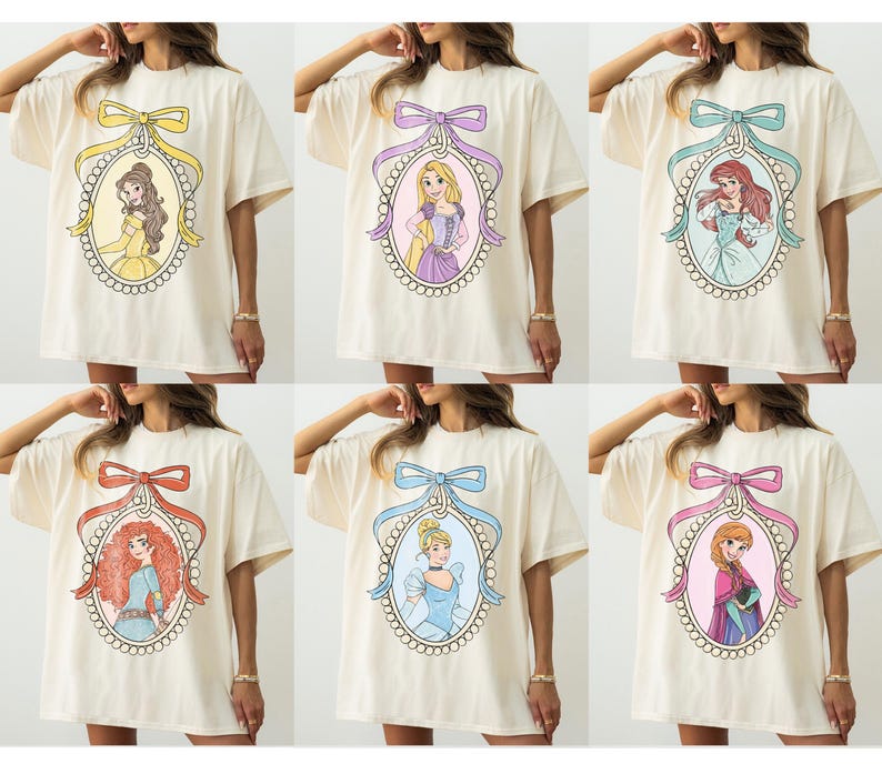 May include: Cream-colored oversized t-shirts featuring cartoon portraits of Disney princesses within ornate oval frames. Each frame is topped with a decorative bow in various colors, including yellow, purple, teal, red, blue, and pink.