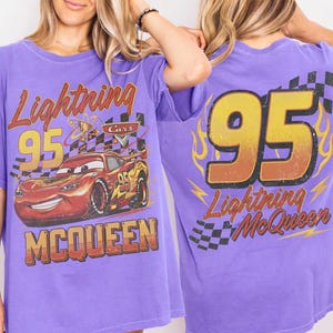 Puede incluir: Camiseta morada con Lightning McQueen de la pel&iacute;cula Cars. El dise&ntilde;o frontal incluye "Lightning 95 McQueen" y una imagen del coche. La parte trasera muestra un gran "95" con "Lightning McQueen" debajo.