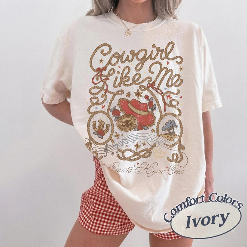 Puede incluir: Una camiseta de manga corta color marfil con un estampado gr&aacute;fico que incluye el texto Cowgirl Like Me y One to Know One. El dise&ntilde;o presenta un sombrero de vaquero rojo, una herradura, un borde de cuerda, notas musicales y estrellas.
