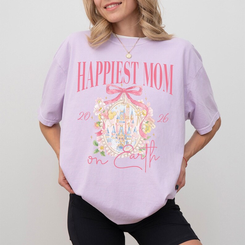 May include: A light purple t-shirt with the text "Happiest Mom" in pink. The shirt features a castle graphic with floral accents and the words "on Earth". The shirt is a casual style.