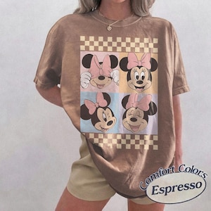 May include: Espresso-colored t-shirt featuring a four-panel graphic of Minnie Mouse faces with pink bows. The design is set against pastel backgrounds and a checkered border. The shirt has short sleeves and the words "Comfort Colors Espresso" are printed on the bottom right.