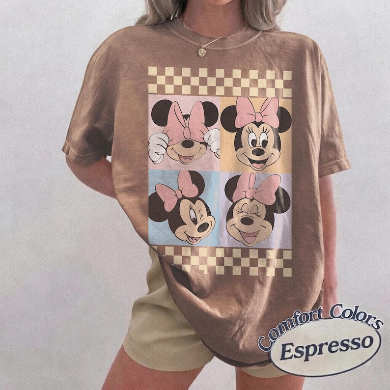 May include: Espresso-colored t-shirt featuring a four-panel graphic of Minnie Mouse faces with pink bows. The design is set against pastel backgrounds and a checkered border. The shirt has short sleeves and the words "Comfort Colors Espresso" are printed on the bottom right.
