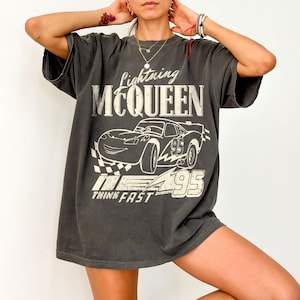 May include: Dark grey t-shirt with a graphic of Lightning McQueen from the Cars film. The design includes the text "Lightning McQueen", a drawing of the car, the number "95", and the words "Think Fast".