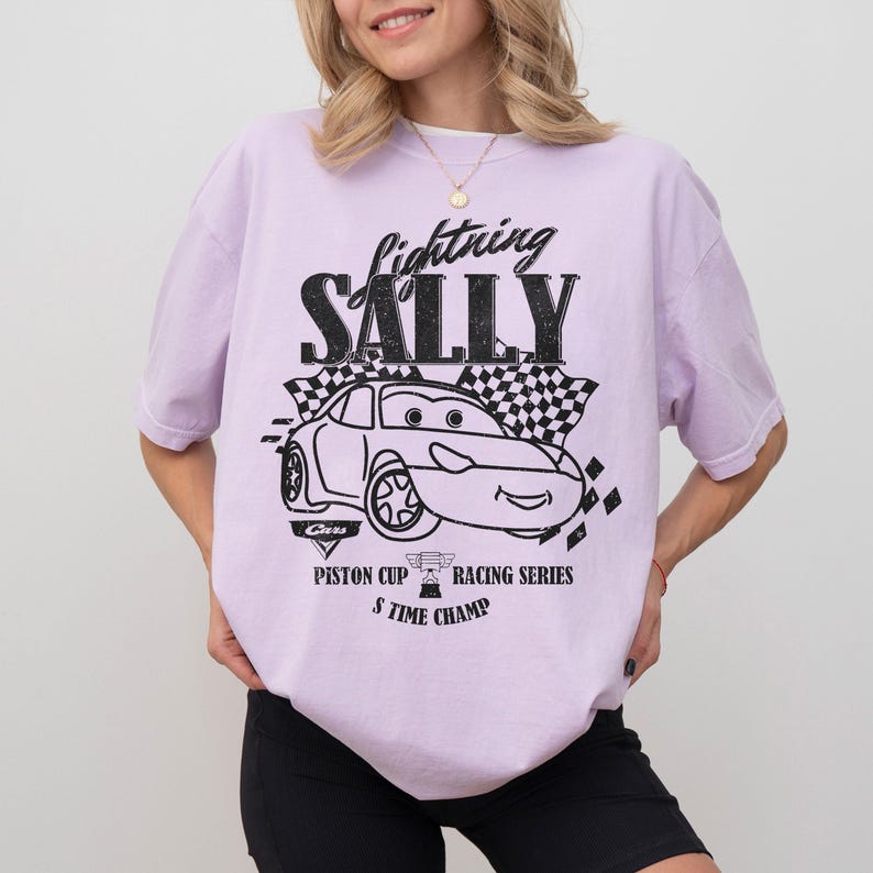 May include: A lilac t-shirt with a black and white graphic of a cartoon car and the text "Lightning Sally". The design includes a checkered flag and the words "Piston Cup Racing Series 5 Time Champ".