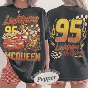 Puede incluir: Camiseta gris oscuro con Lightning McQueen de la pel&iacute;cula Cars. El gr&aacute;fico frontal muestra a McQueen con el n&uacute;mero 95, una bandera a cuadros y el texto "Lightning McQueen". La parte trasera muestra un gran "95" con llamas y el texto "Lightning McQueen".