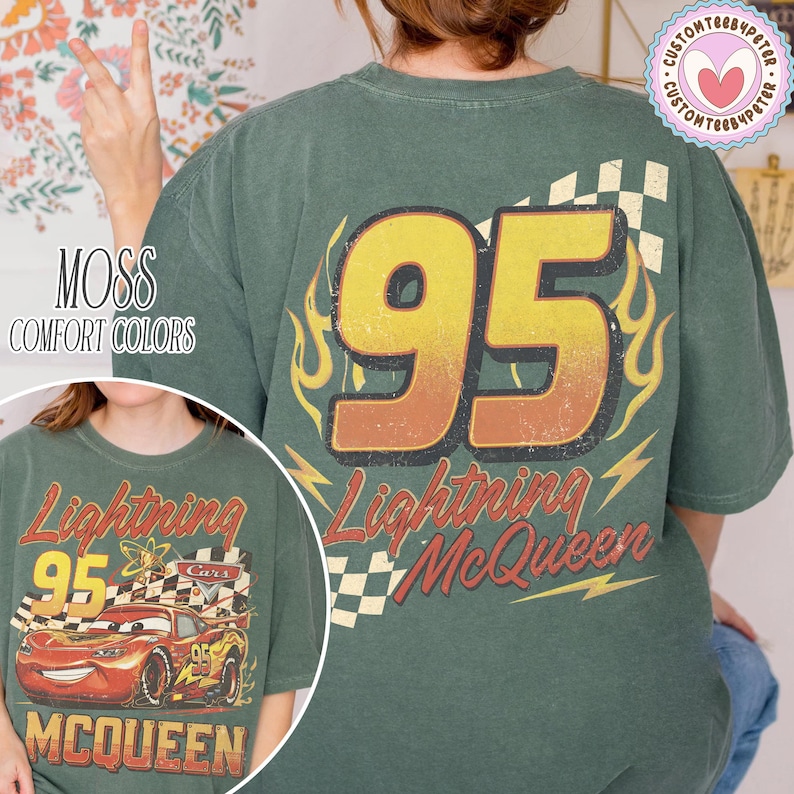 Puede incluir: Camiseta verde con un gran n&uacute;mero 95 en amarillo y naranja, gr&aacute;ficos de llamas y rayos, y el texto "Lightning McQueen". La camiseta tambi&eacute;n tiene el texto "MOSS COMFORT COLORS".