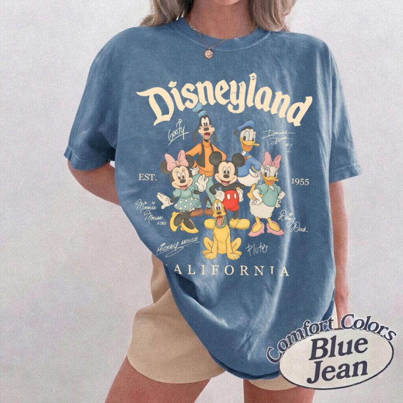 K&ouml;nnte beinhalten: Ein blaues Kurzarm-T-Shirt mit einem Grafikdruck von Disney-Figuren, darunter Mickey Maus, Minnie Maus, Donald Duck, Daisy Duck, Goofy und Pluto. Der Text lautet Disneyland, Est. 1955, California, und enth&auml;lt die Unterschriften der Figuren.