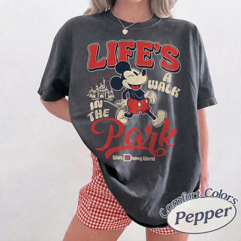 May include: Dark grey t-shirt with Mickey Mouse graphic and the text "Life's a Walk in the Park" in red and white. The shirt also includes "Walt Disney World" and a castle graphic. The shirt is a Comfort Colors brand.