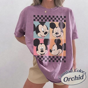 May include: Purple Comfort Colors t-shirt featuring four Mickey Mouse faces in a grid pattern with a checkered border. The shirt has the words "Comfort Colors" and "Orchid" printed on the bottom right.