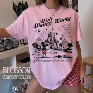 Peut inclure: T-shirt rose clair avec un dessin noir du ch&acirc;teau de Walt Disney World, Mickey Mouse et des feux d'artifice. Le texte sur le t-shirt indique "Walt Disney World" et "The happiest place on earth."