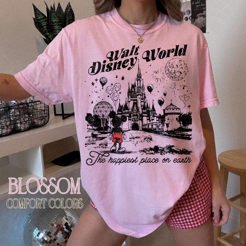 Peut inclure: T-shirt rose clair avec un dessin noir du ch&acirc;teau de Walt Disney World, Mickey Mouse et des feux d'artifice. Le texte sur le t-shirt indique "Walt Disney World" et "The happiest place on earth."