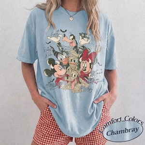 May include: Pale blue Comfort Colors Chambray t-shirt with a graphic of Disney characters, including Mickey and Minnie Mouse, Donald Duck, and Goofy. The graphic includes character signatures and the word "Pluto".