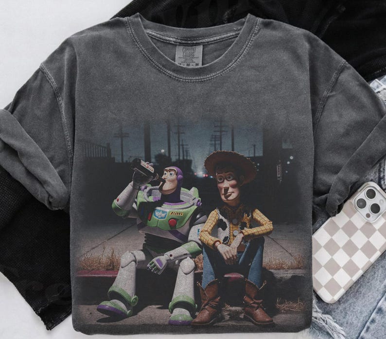 May include: Dark grey long-sleeve shirt with a graphic of Buzz Lightyear and Woody from Toy Story. Buzz is drinking from a bottle, and Woody is sitting beside him. The image has a distressed, vintage appearance.