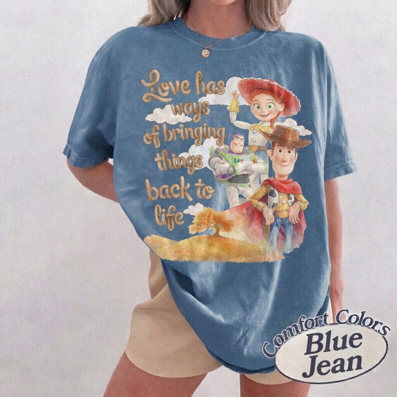 K&ouml;nnte beinhalten: Ein blaues Kurzarm-T-Shirt mit einem Grafikdruck von Toy Story-Figuren, darunter Woody, Buzz Lightyear und Jessie. Der Text lautet, Love has ways of bringing things back to life. Das T-Shirt hat einen Rundhalsausschnitt und eine lockere Passform.