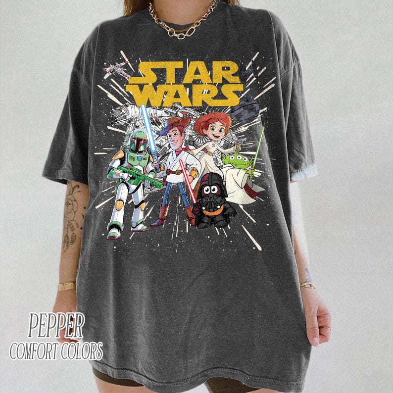 Puede incluir: Camiseta gris oscuro con el logotipo de Star Wars y personajes de dibujos animados como Boba Fett, Woody, Jessie, Darth Vader y un extraterrestre. La camiseta est&aacute; estampada con un efecto desgastado y el texto "Pepper Comfort Colors".