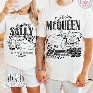May include: Ivory t-shirts with Lightning McQueen and Sally Carrera designs from the Cars film. The black graphics include the characters, racing flags, and text. The text reads "Piston Cup Racing Series" and "Think Fast".