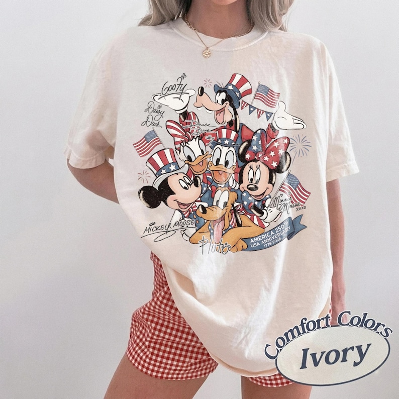 Puede incluir: Camiseta Comfort Colors color marfil con un dise&ntilde;o patri&oacute;tico con Mickey Mouse, Minnie Mouse, Donald Duck, Daisy Duck, Goofy y Pluto. El gr&aacute;fico incluye banderas americanas y texto que celebra el 250 aniversario de Am&eacute;rica.