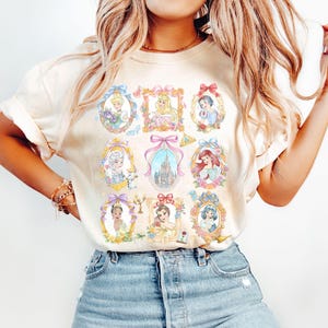 Pu&ograve; includere: T-shirt color crema con ritratti incorniciati di principesse animate. Ogni ritratto &egrave; circondato da decorazioni floreali e nastri. La maglietta &egrave; realizzata in un materiale morbido e ha maniche corte.