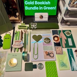 May include: A collection of green stationery items including a daily planner, pens, a pencil case, a hair scrunchie, stickers, a bookmark, and various office supplies. A tablet screen displays the text Gold Bookish Bundle in Green.