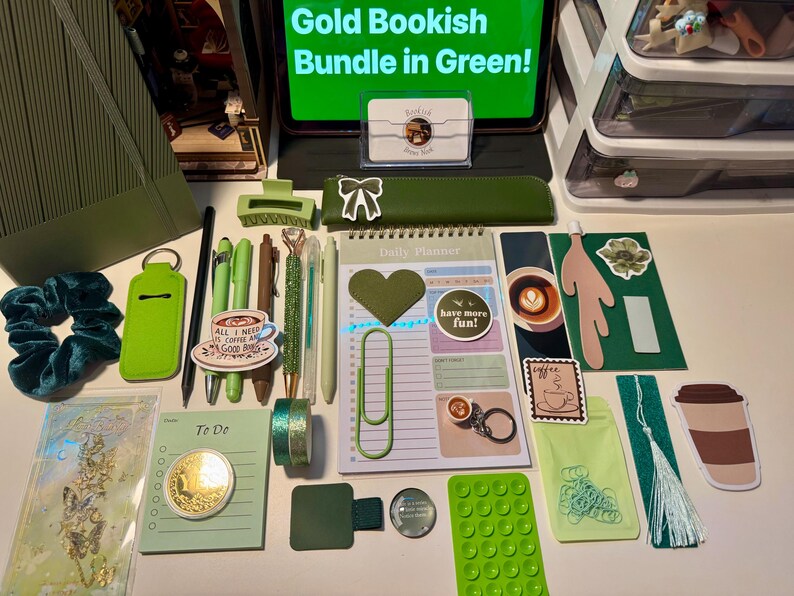 May include: A collection of green stationery items including a daily planner, pens, a pencil case, a hair scrunchie, stickers, a bookmark, and various office supplies. A tablet screen displays the text Gold Bookish Bundle in Green.