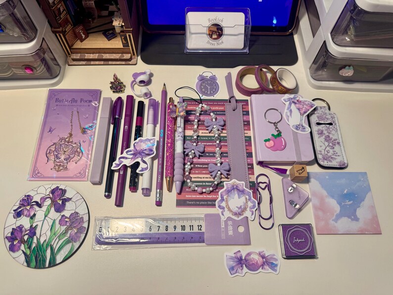 May include: A collection of purple stationery items including a notebook, pens, pencils, a 12-centimeter ruler, washi tape, stickers, a beaded lanyard with bows, a keychain, a stamp, and a circular coaster featuring a purple iris flower illustration.