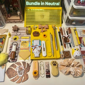 May include: A collection of yellow-themed stationery and accessories including a yellow notebook, pens, markers, a yellow pencil case, sunflower-themed clips, a cow sticker, a plush heart keychain, a velvet scrunchie, and various decorative paper items.