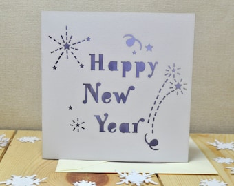 Può includere: Carta bianca con un messaggio "Happy New Year" in viola e un design di fuochi d'artificio ritagliato.