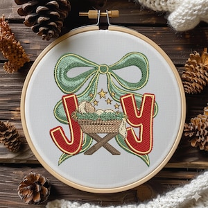 May include: Embroidered hoop art featuring the word "JOY" in red with gold trim. A green bow and a manger scene with stars are embroidered above the word. The artwork is set in a wooden embroidery hoop.