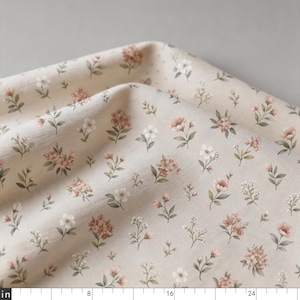 May include: Close-up of a beige fabric with a delicate floral pattern. The design features small, scattered flowers in shades of pink and white, with green leaves. The fabric is folded, showing its texture.