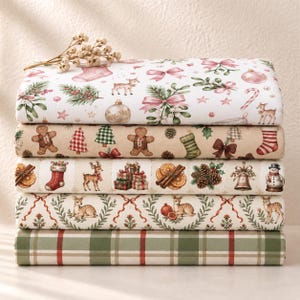 Peut inclure: Une pile de cinq rouleaux de tissu pliés avec des motifs de fête. Le rouleau supérieur présente des nœuds roses et des cerfs sur fond blanc. Le deuxième a des bonshommes en pain d'épice et des chaussettes sur fond beige. Le troisième a des cadeaux et des pommes de pin. Le quatrième a des cerfs et de la verdure. Le bas est à carreaux verts.