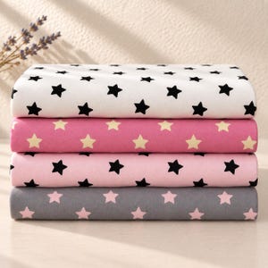 May include: A stack of four folded fabric pieces featuring star patterns. The top piece is white with black stars, the second is dark pink with light yellow stars, the third is light pink with black stars, and the bottom is grey with light pink stars.