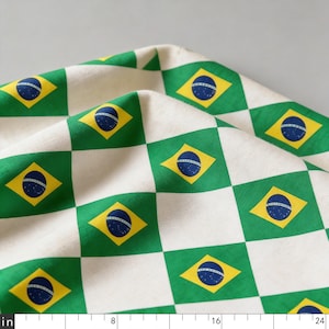 May include: A folded piece of fabric featuring a repeating diamond pattern of the Brazilian flag, with green, yellow, and blue colours. A white ruler at the bottom shows measurements in inches, ranging from 0 to 24 inches across the bottom edge.