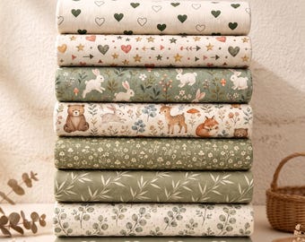 May include: A stack of eight folded fabric bolts featuring various patterns including green hearts, stars and arrows, white rabbits in a forest, woodland animals like bears and deer, small floral prints, and green leaves on cream and sage green backgrounds.