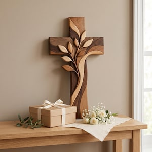 May include: A wall-mounted wooden cross featuring a layered, multi-toned design with dark and light brown wood grain. A carved branch with smooth, stylized leaves extends diagonally across the center of the cross, adding depth and texture.