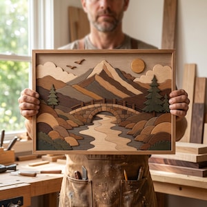 Op de afbeelding: Een rechthoekig houten wandkunstwerk met een gelaagd landschapsontwerp. De afbeelding toont een stenen brug over een kronkelende rivier, omringd door glooiende heuvels, groenblijvende bomen, wolken, een ronde zon en twee vogels in de lucht.