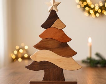 May include: A decorative wooden Christmas tree sculpture composed of five stacked, wavy horizontal segments in varying shades of brown and tan wood, topped with a light-colored wooden star and mounted on a rectangular wooden base.