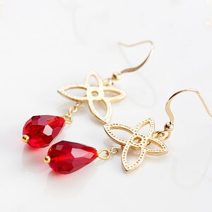 Op de afbeelding: Gouden oorbellen met een delicaat vierpuntig sterontwerp en hangende rode druppelkristallen.