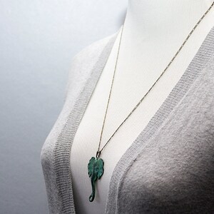 May include: A silver chain necklace with a green elephant pendant. The necklace is on a gray sweater.