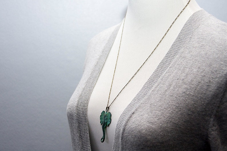 May include: A silver chain necklace with a green elephant pendant. The necklace is on a gray sweater.